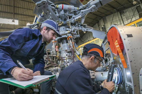 Two men who are engineers looking at a machine and one of the men has a clipboard and is taking notes