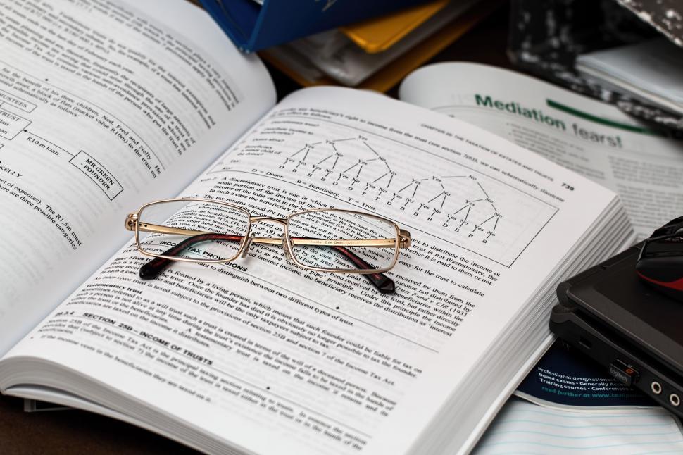 Image displays reading glasses resting on a mathematics guidebook used in compliance and risk apprenticeship training.